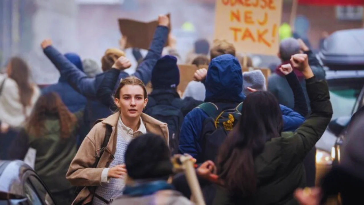 Young woman walks through protest crowd during evacuation scene in Netflix’s Families Like Ours.