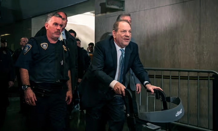 Harvey Weinstein escorted by officers in courtroom hall, appearing frail during retrial hearings.