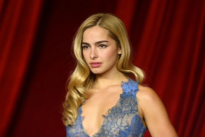 Addison Rae portrait with long blonde waves, minimal makeup, and a lace-accented light-blue evening dress.