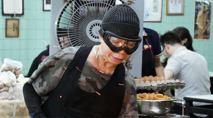 Jay Fai wears goggles while cooking in her Bangkok kitchen, known for her fiery street food dishes