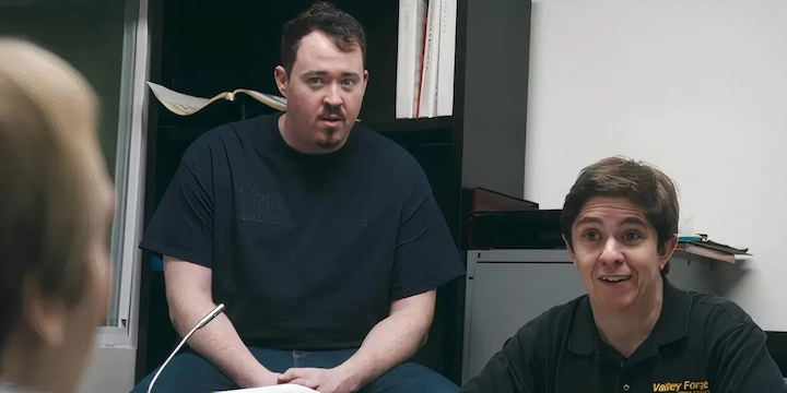 Two shop employees intently listening to a customer in office with papers and computer behind them.
