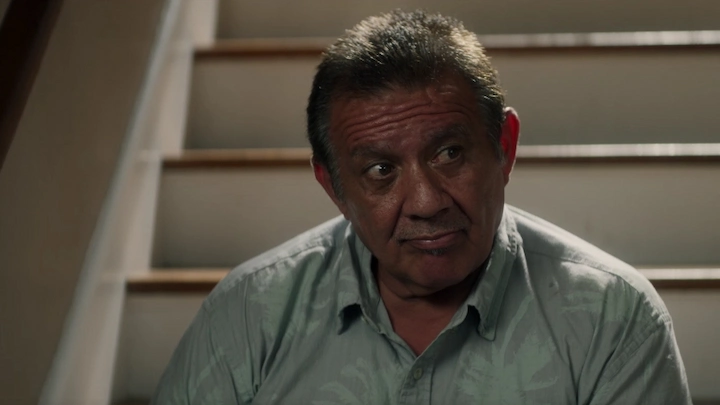 Older Johnny Pollerana sitting on stairs, reflecting on his past as David Sconce’s trusted right-hand man.