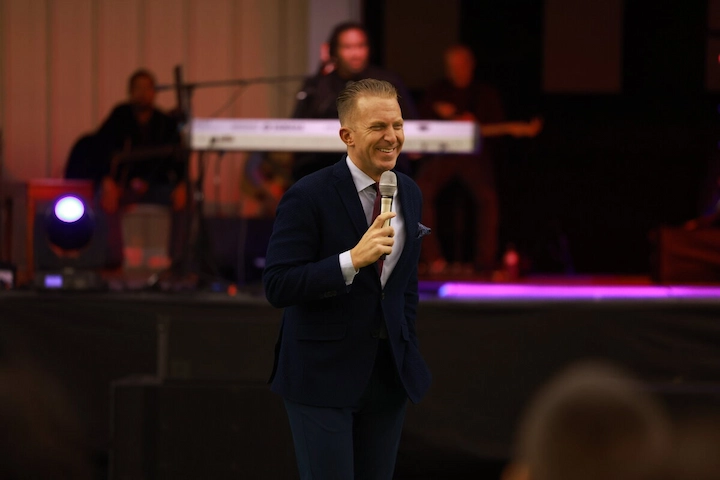Jonathan Shuttlesworth speaking at a church event, holding a microphone in a navy suit.