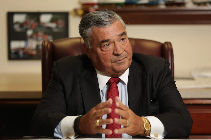 Joseph Sanzari in a business suit and red tie seated at his office desk, showing leadership and success