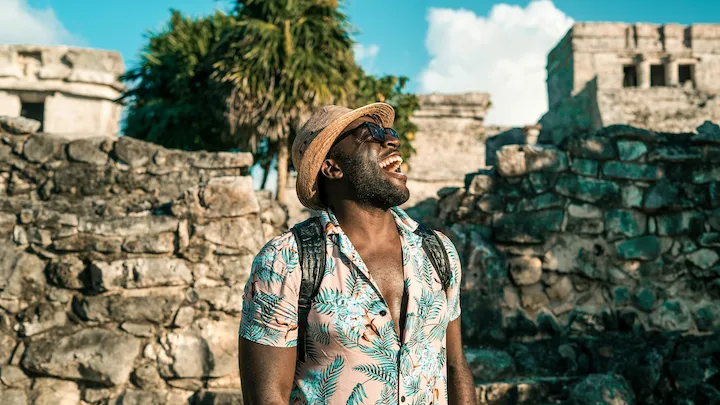 Jubril Agoro exploring ancient ruins, wearing a hat and tropical shirt, embracing global travel life.