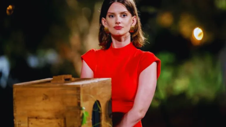 Kathryn Cavender in red dress standing beside a wooden box during a dramatic film scene.