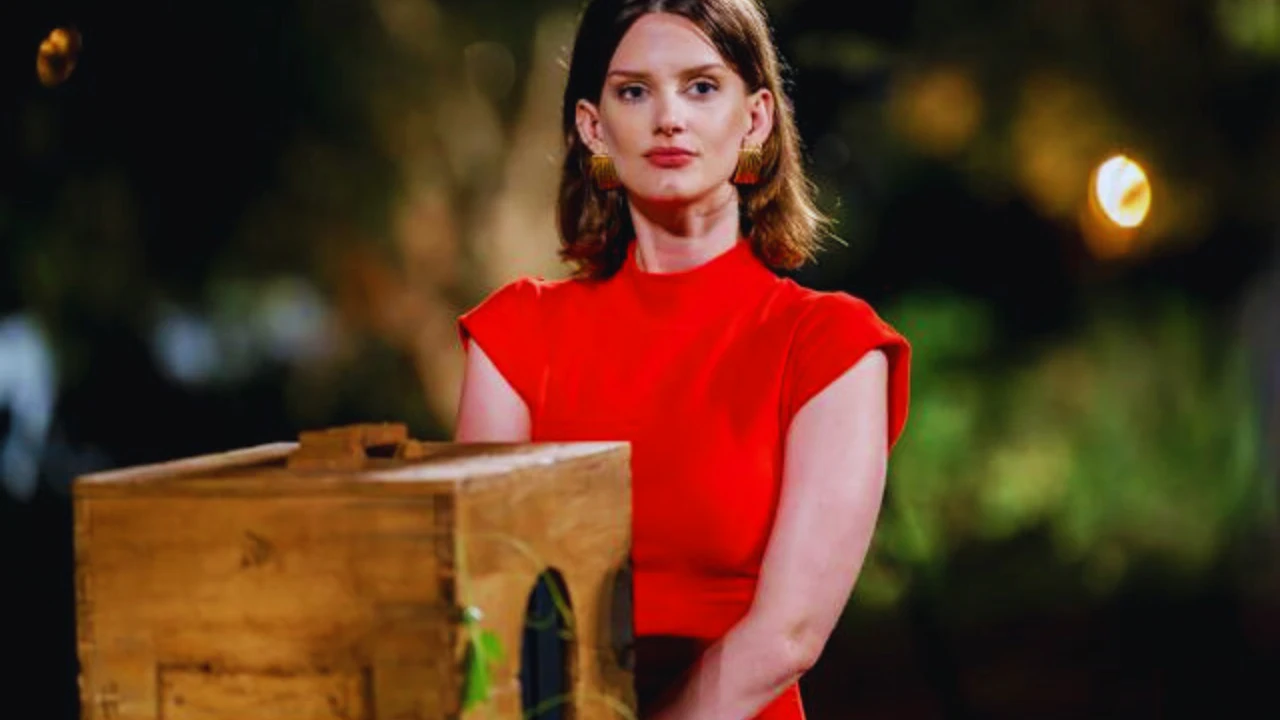 Kathryn Cavender in red dress standing beside a wooden box during a dramatic film scene.