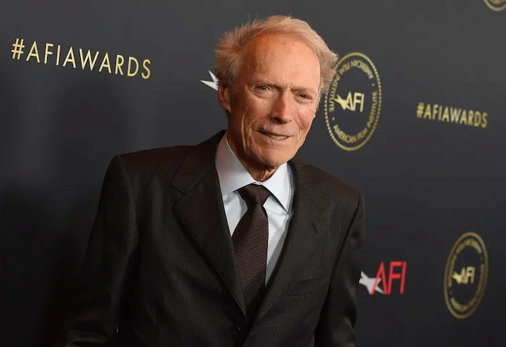 Clint Eastwood posing on the AFI Awards red carpet, dressed in a black suit, smiling at photographers.