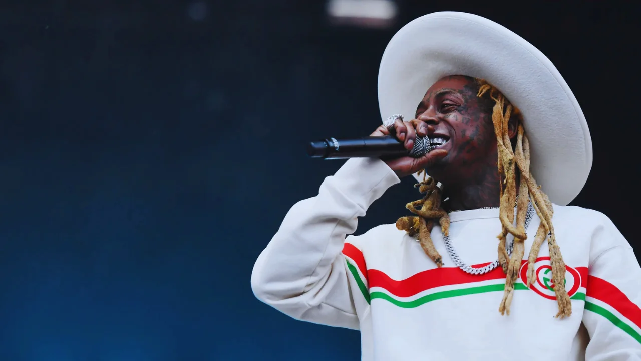 Lil Wayne performing live on stage in a white hat and sweatshirt during Tha Carter VI Tour 2025.