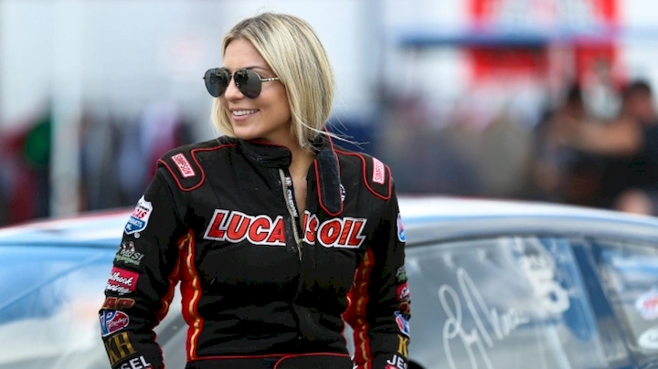 Lizzy Musi in a racing suit standing by her car at a motorsport event, showcasing her racing career.