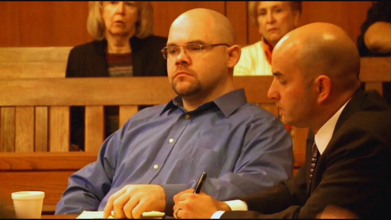Louis Mann sits in court during murder trial with defense attorney, courtroom audience in background.