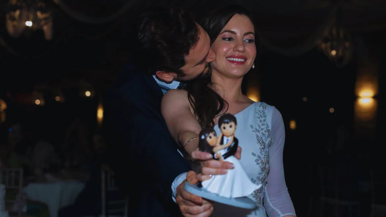 Bride and groom smiling at wedding, woman holding cake topper, romantic wedding moment.