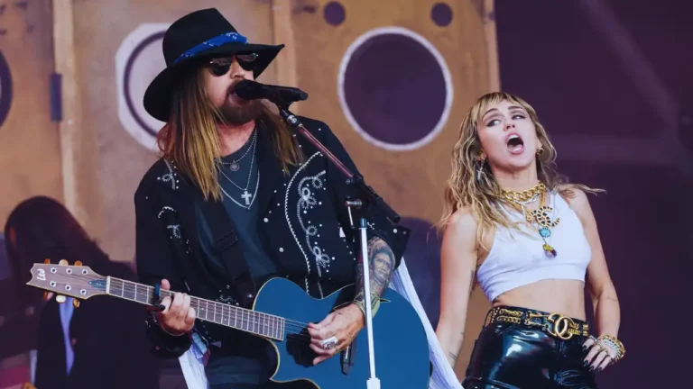 Billy Ray Cyrus and Miley Cyrus perform together on stage with guitar and dynamic stage presence.