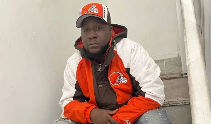 Murda Pain wearing Cleveland Browns jacket and cap while sitting on stairs, casual and relaxed pose