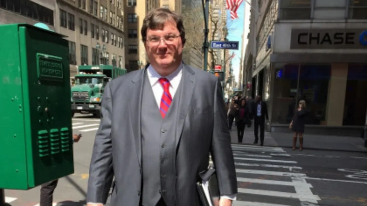 Rex Heuermann smiling in a gray suit and red tie, walking on a New York City street near 46th Street.