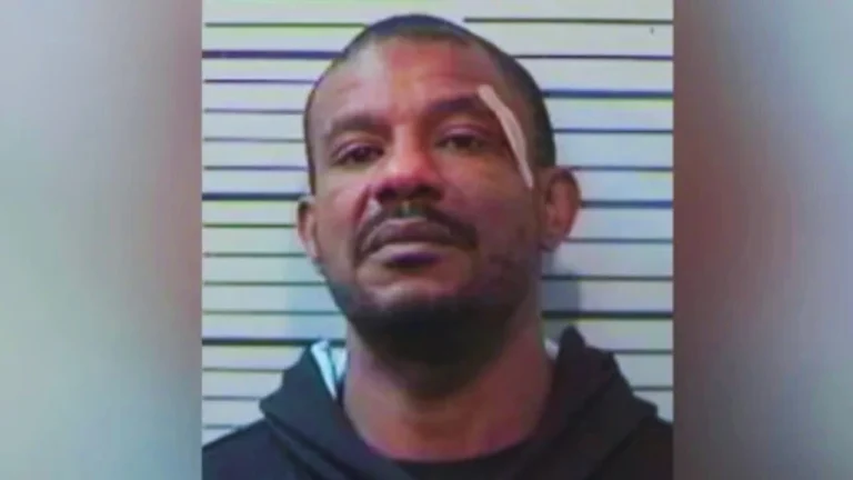 Mugshot of a man with close-cropped hair and bandage above his eye against height lines.