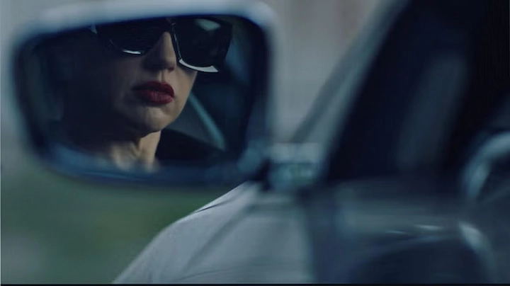 Mirror image of a focused woman wearing sunglasses, red lipstick, highlighting her determined gaze.