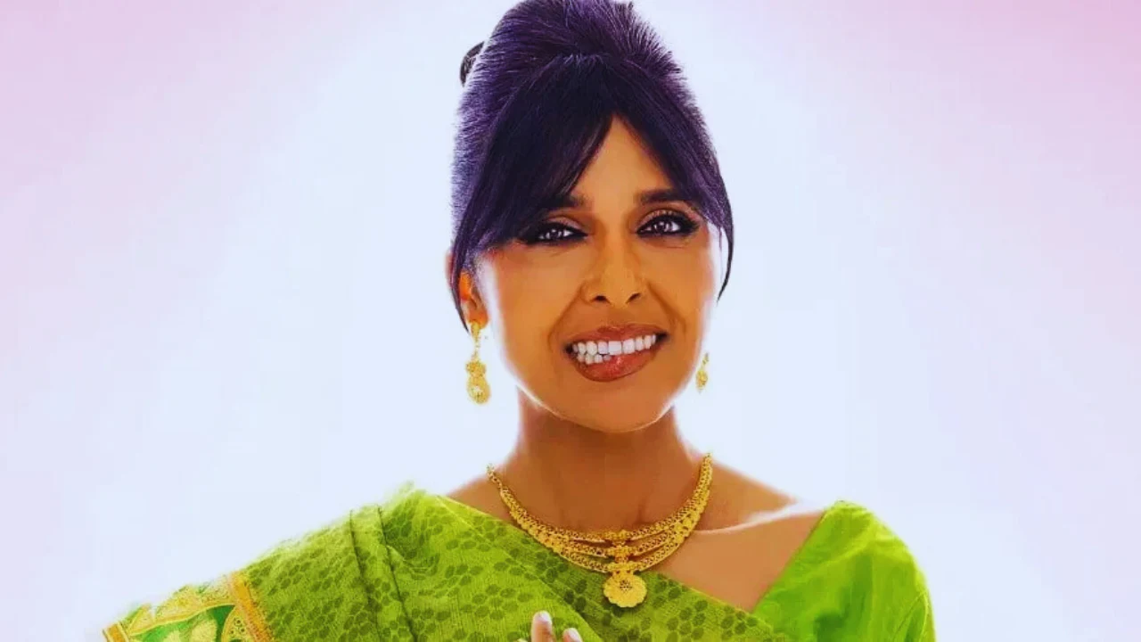 Indian-American woman in green saree smiling with gold jewelry on pink background.