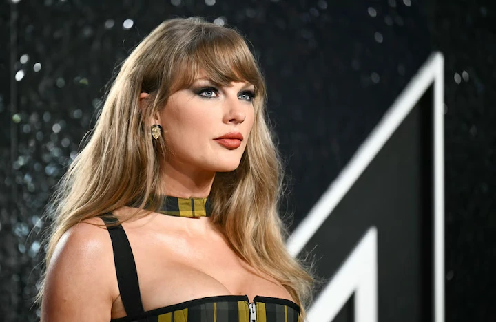 Taylor Swift poses confidently at red carpet event in a striped dress and bold makeup look.