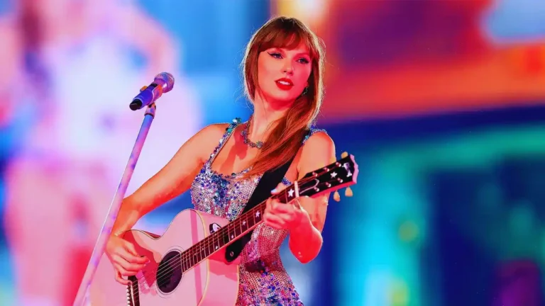 Taylor Swift performs live on stage in a sparkling dress while playing acoustic guitar.