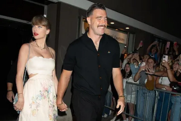 Taylor Swift and Travis Kelce hold hands leaving a wedding venue, Swift in white floral skirt, Kelce in black shirt.