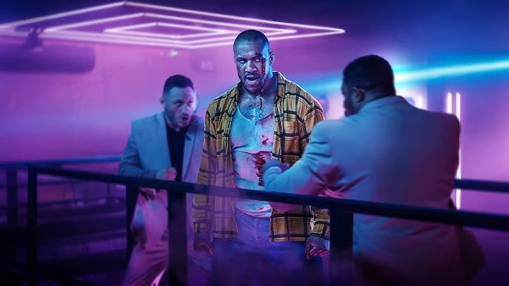 Bastien fights gang thugs in a neon-lit club, fiercely defending Léo amid chaos and flying punches.