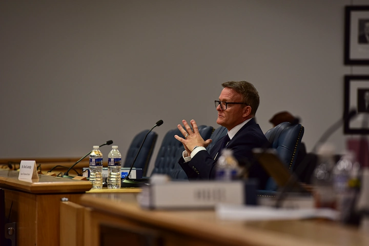 David Lochridge testifying at a hearing, seated in a formal room with microphones and papers.