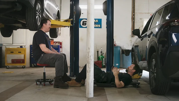 Four Valley Forge Automotive Center mechanics standing behind a tire display in their garage smiling.