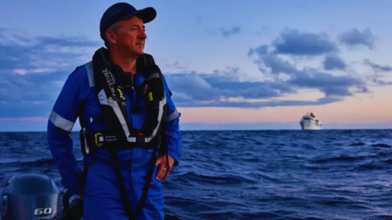 Rob McCallum stands on a boat in full gear during deep-sea expedition at sunset.