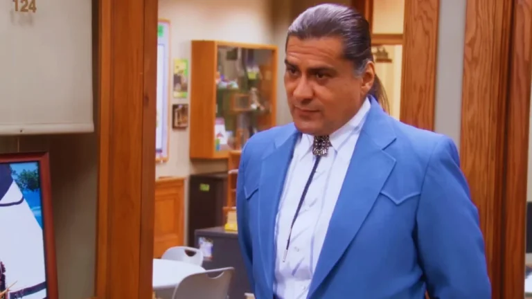 Jonathan Joss as Chief Ken Hotate in a Parks and Recreation scene, wearing a blue suit and bolo tie.