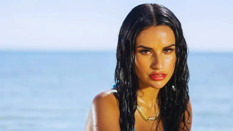Yulissa Escobar poses wet-haired in a blue swimsuit by the ocean shore on the Love Island USA villa set.