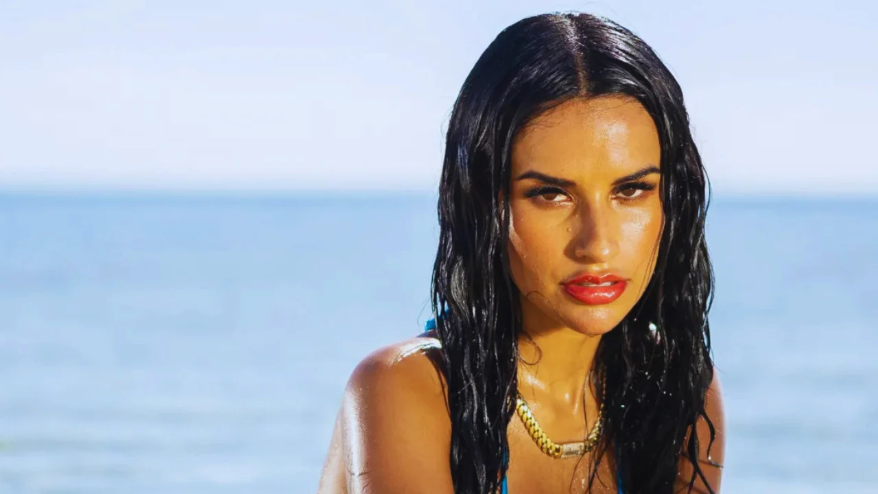 Yulissa Escobar poses wet-haired in a blue swimsuit by the ocean shore on the Love Island USA villa set.